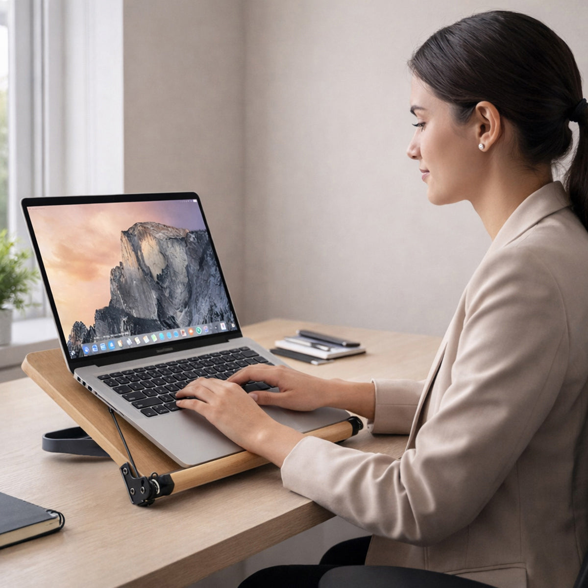 Mujer trabajando en su escritorio utilizando el soporte de madera junto a su laptop para mejorar su postura y mantener un espacio de estudio organizado